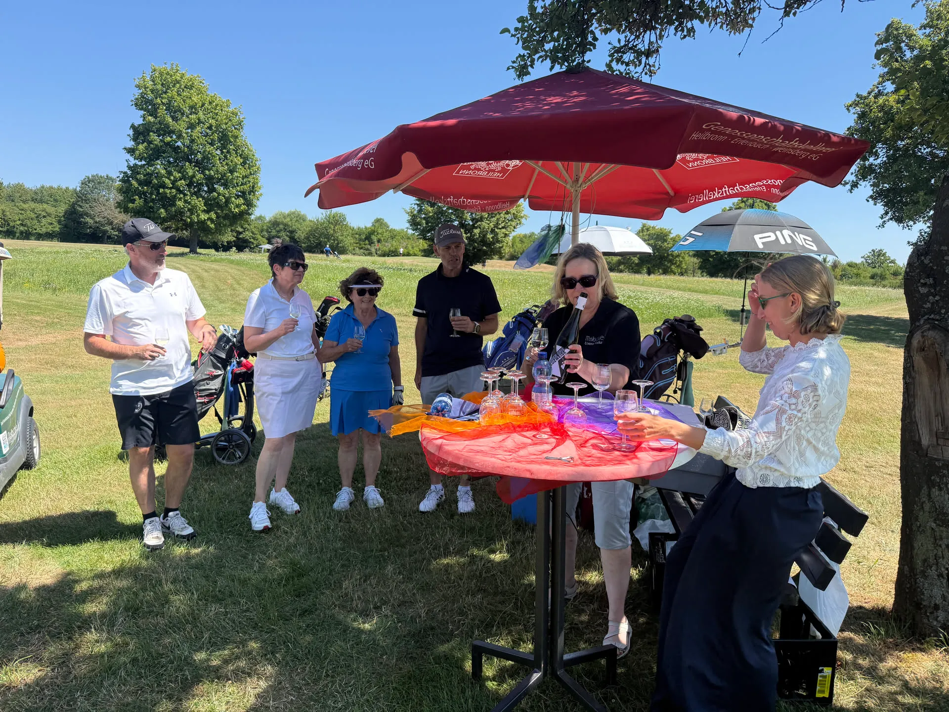 Weinprobe unter einem roten Sonnenschirm auf dem Golfplatz